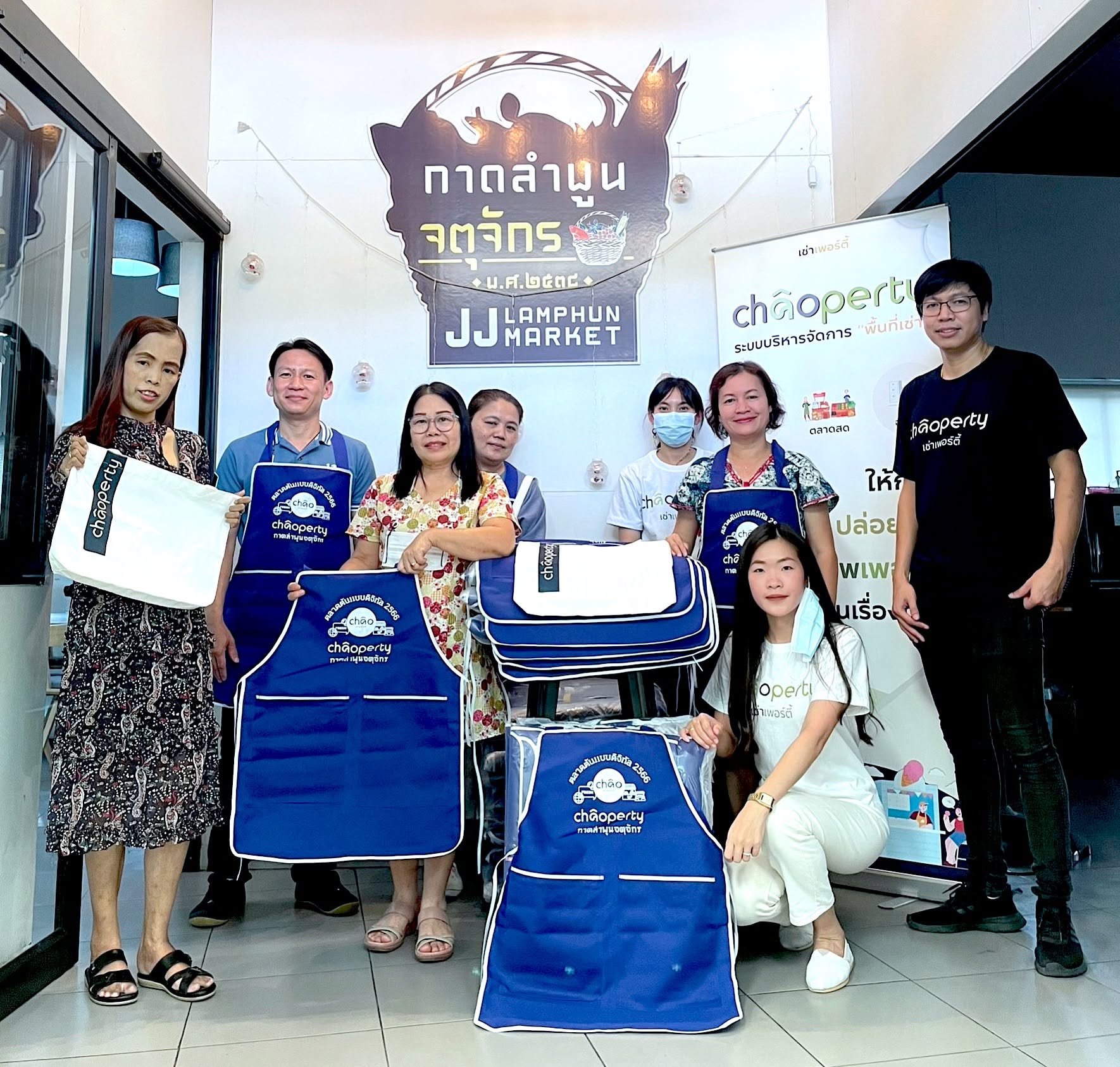 ทีมงานและแม่ค้าที่กาดลำพูนจตุจักรถือผ้ากันเปื้อน Chaoperty